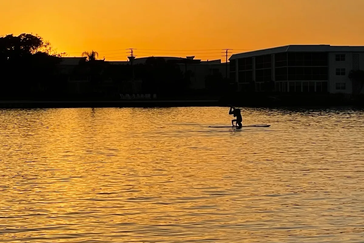 A paddleboarder silhouetted on golden water at sunset on the Intracoastal in Tequesta