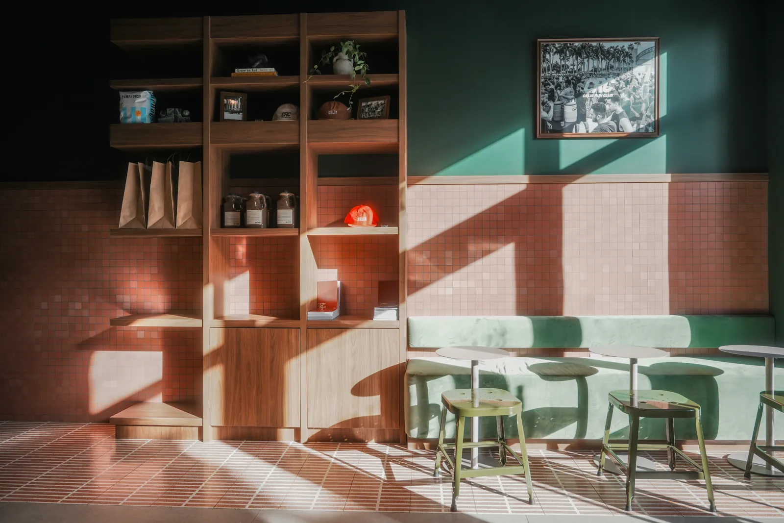 Cafe interior with wooden shelving, terracotta mosaic tile, mint banquette and olive stools in dramatic sunlight