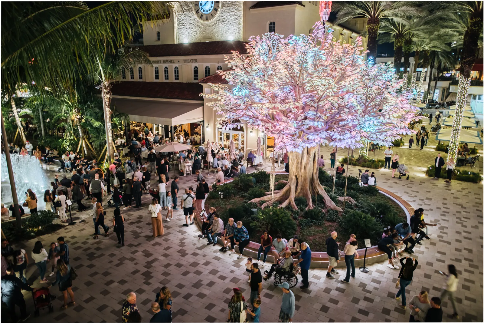 Illuminated glowing tree in a crowded outdoor plaza at night