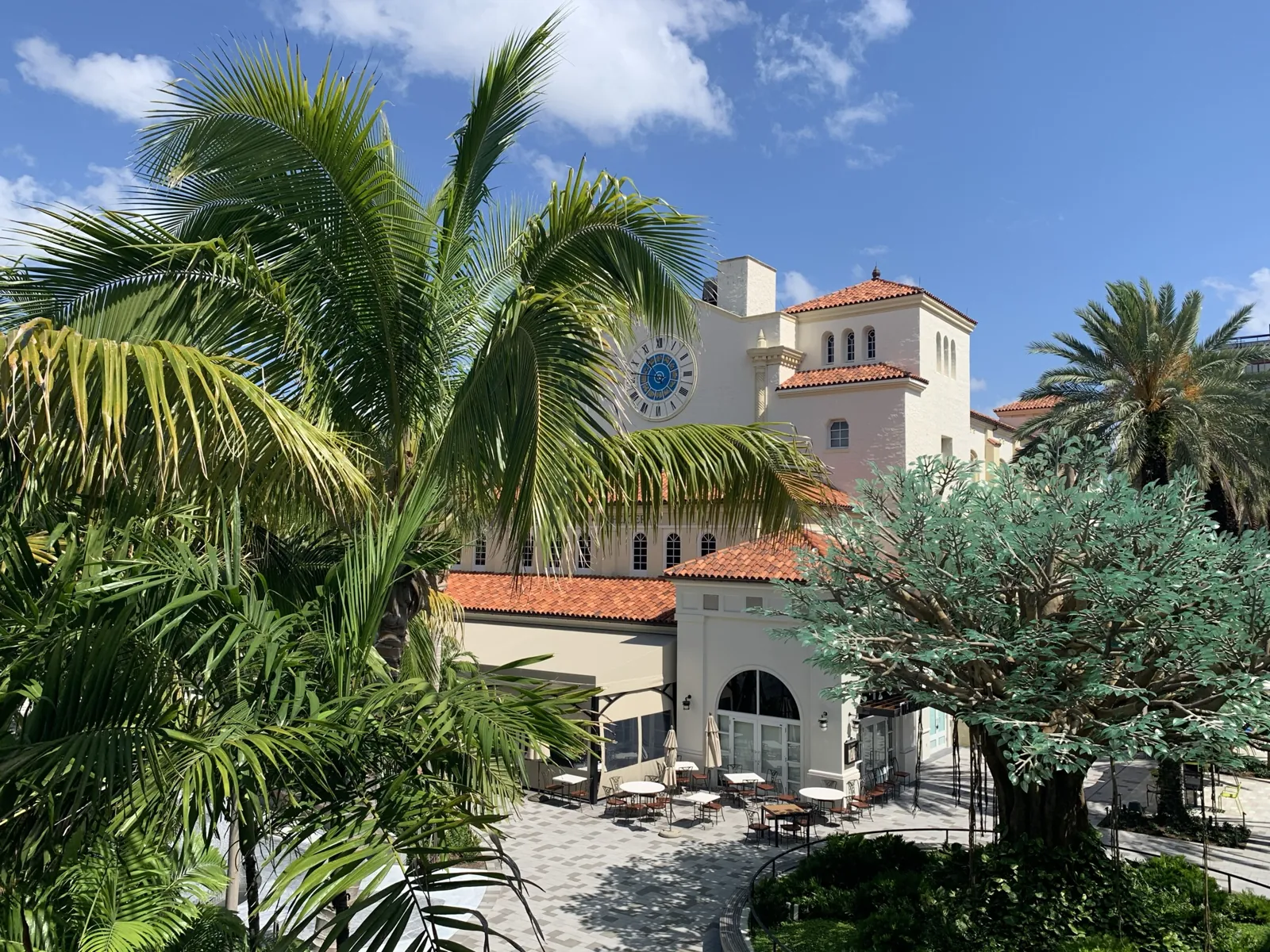 Mediterranean Revival plaza with clock tower, terracotta roofs, and outdoor café patio framed by palms