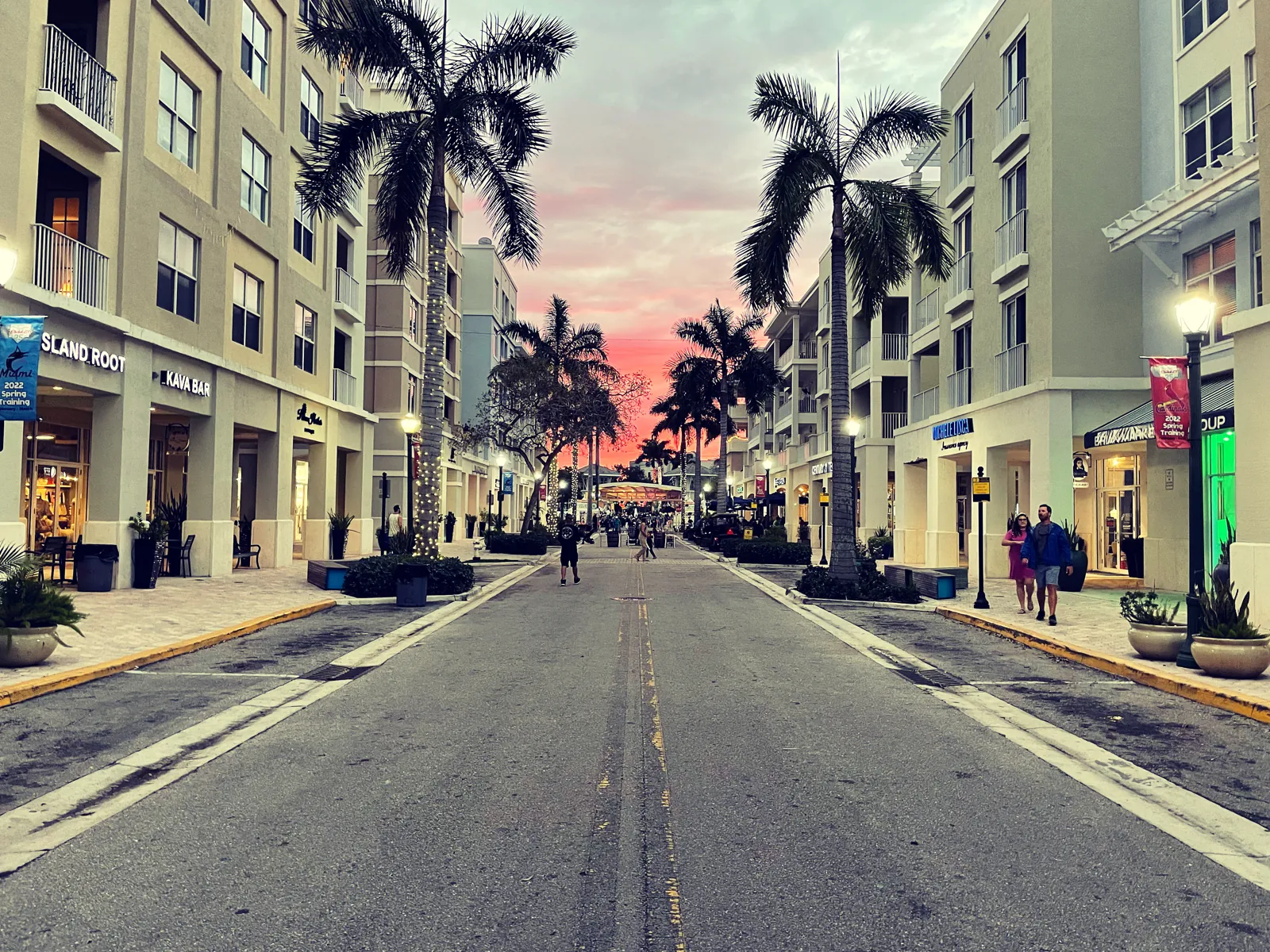 Pedestrian-friendly mixed-use shopping street at sunset, lined with royal palms