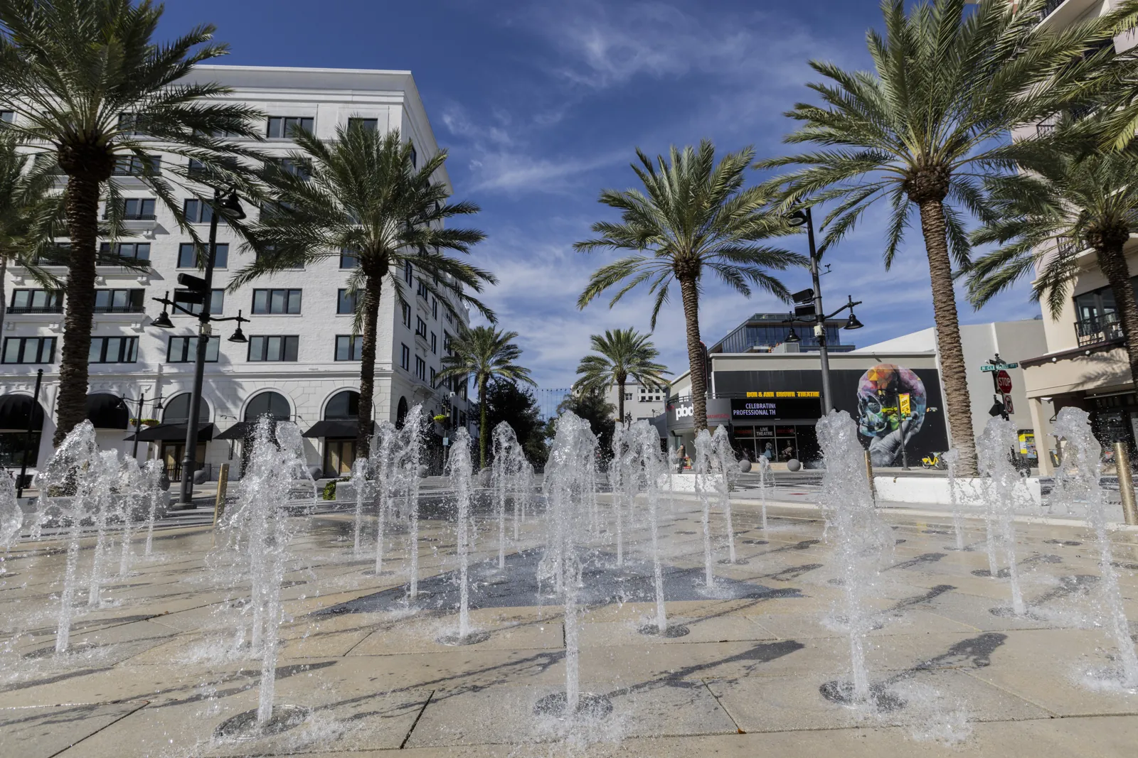 Interactive jet fountain plaza with palm trees and white mixed-use buildings