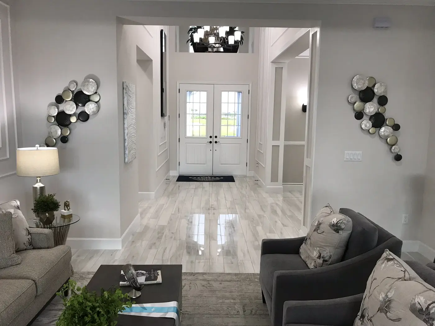 A living room with gray sofas looking toward a tiled entry hall and double front doors in a Minto model home in Westlake