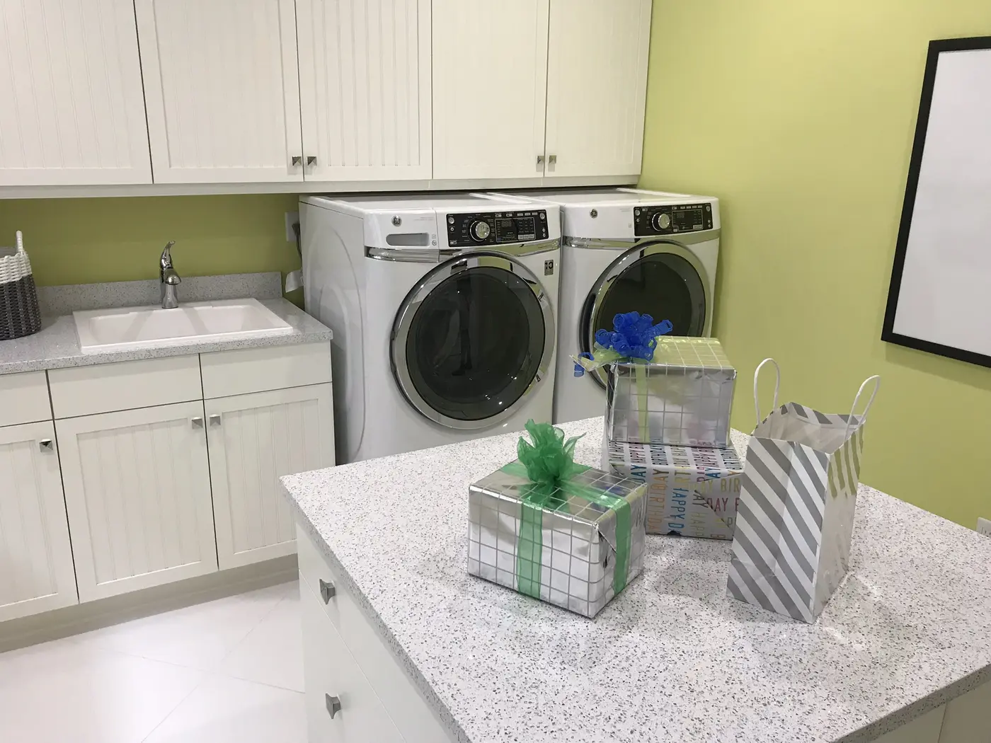 A laundry room with front-loading washer and dryer, white cabinets, a utility sink and a granite-topped island in a Minto model home in Westlake