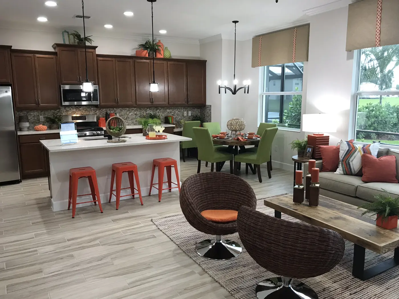 An open kitchen with dark wood cabinets, an island with orange stools, a dining table and a sitting area in a Minto model home in Westlake