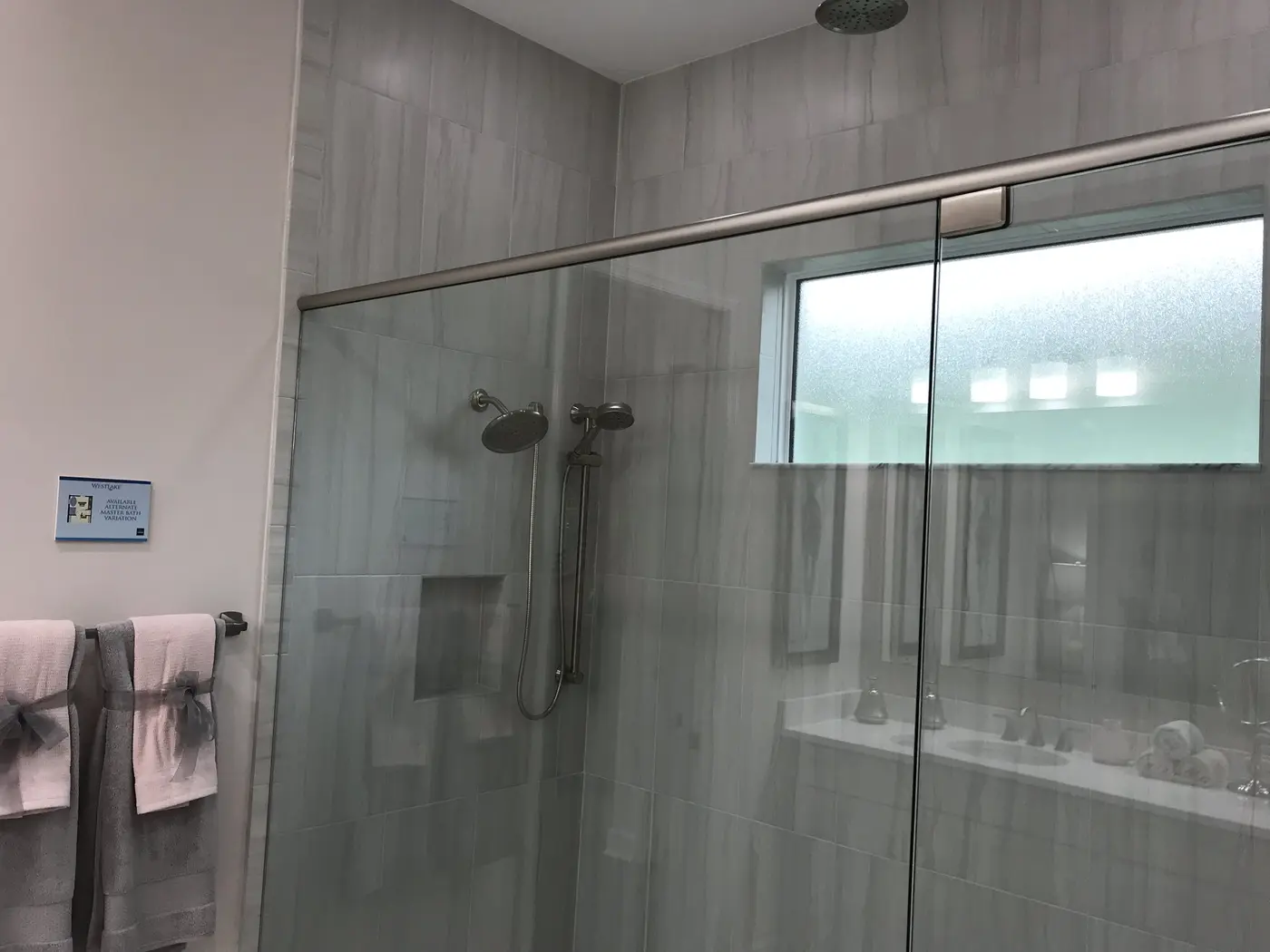 A walk-in shower with a glass enclosure, gray wall tile and a high frosted window in a Minto model home in Westlake