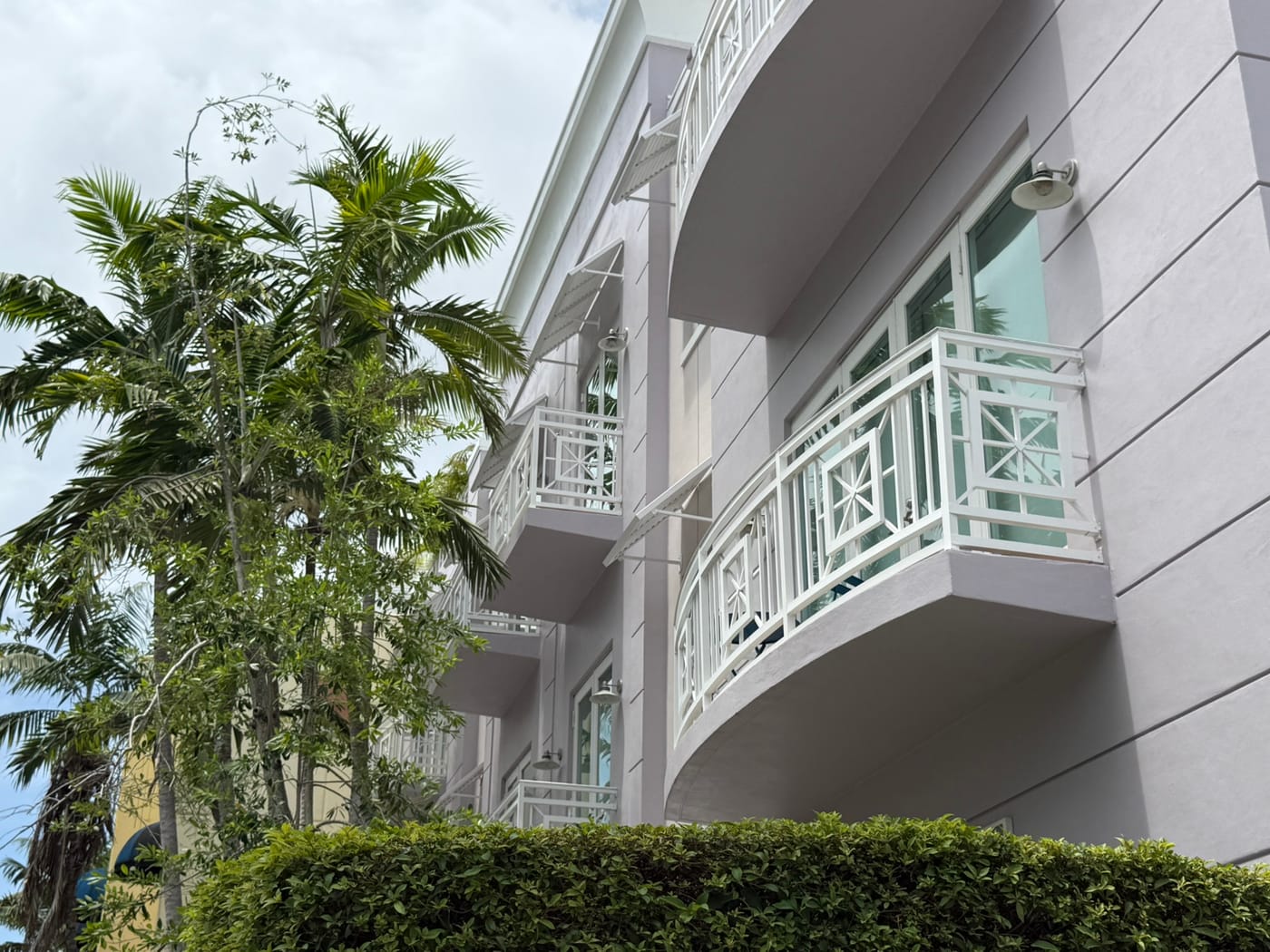 Curved white balconies on a lavender condominium building behind a clipped hedge