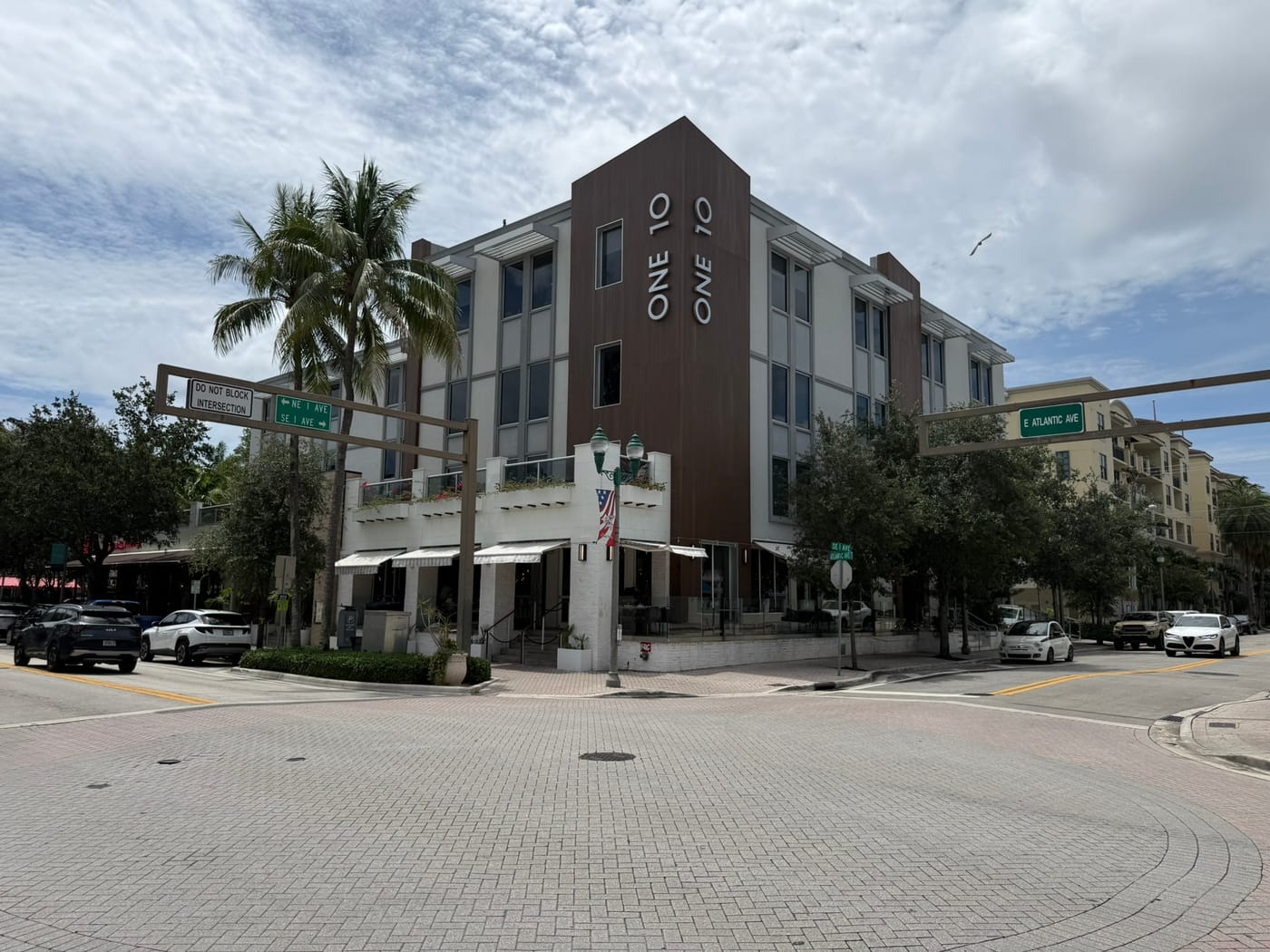 A four-story mixed-use building with ground-floor storefronts on a brick-paved corner