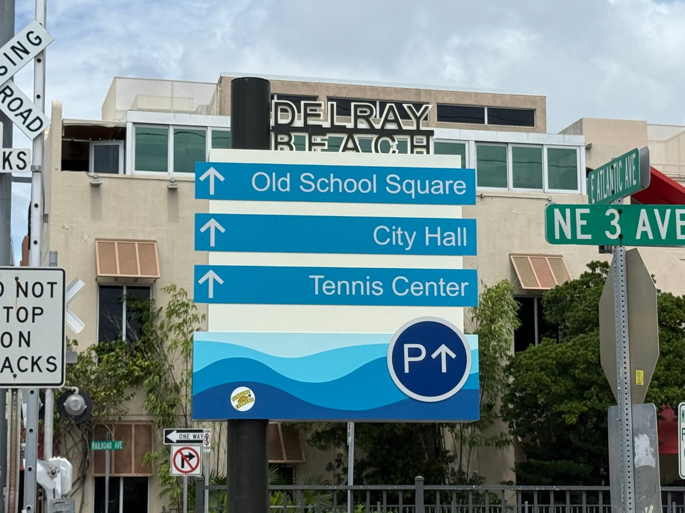A downtown wayfinding sign pointing to Old School Square, City Hall and the Tennis Center, with a public parking symbol