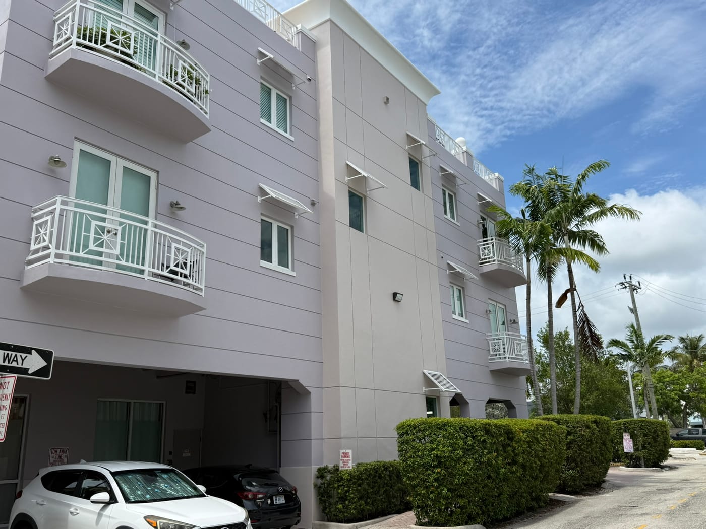 A lavender three-story condominium building with white balconies and covered parking beneath