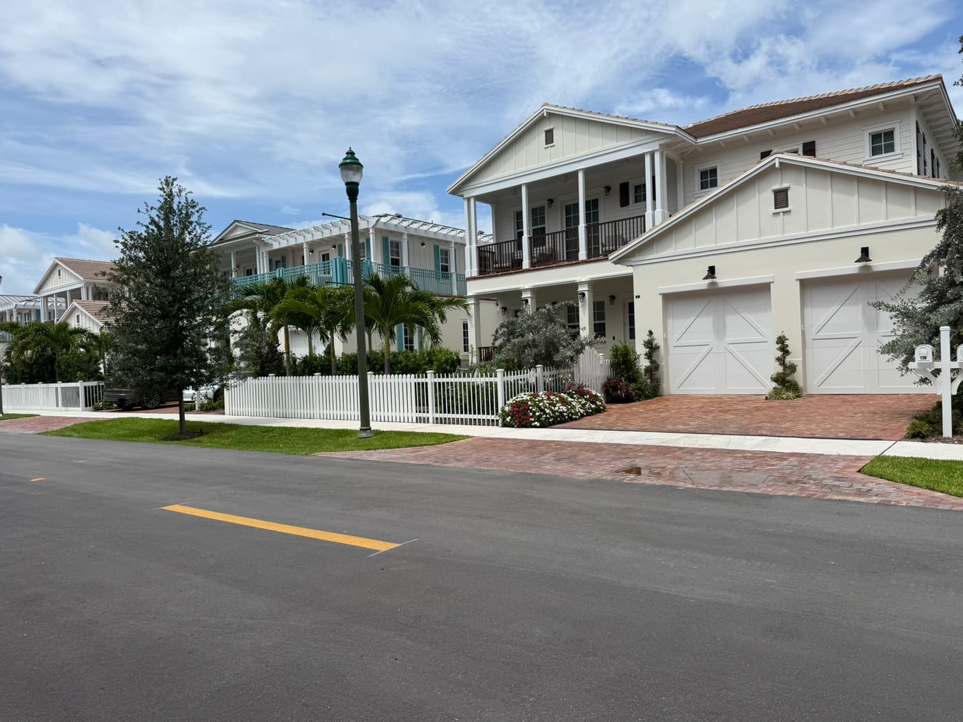A street of newer two-story coastal-style homes with white picket fences, brick driveways and street lamps