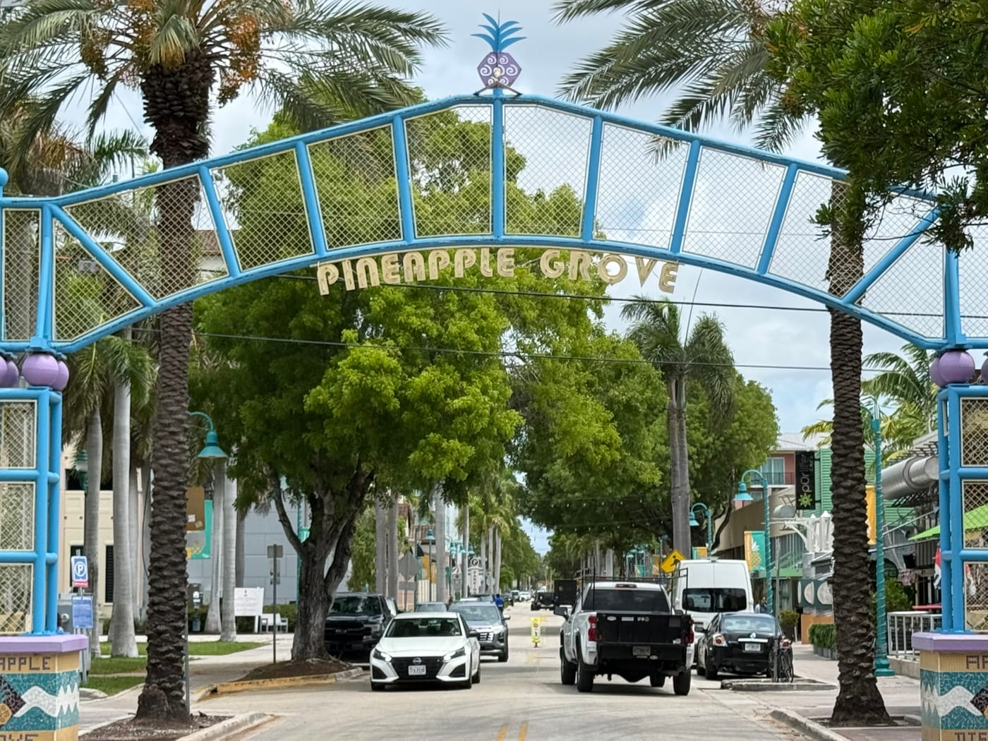 The blue metal Pineapple Grove arch spanning a street, with palms and parked cars beneath it