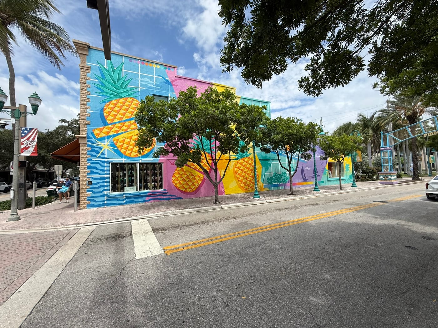 A two-story downtown building painted with a large pineapple mural in blue, pink and yellow