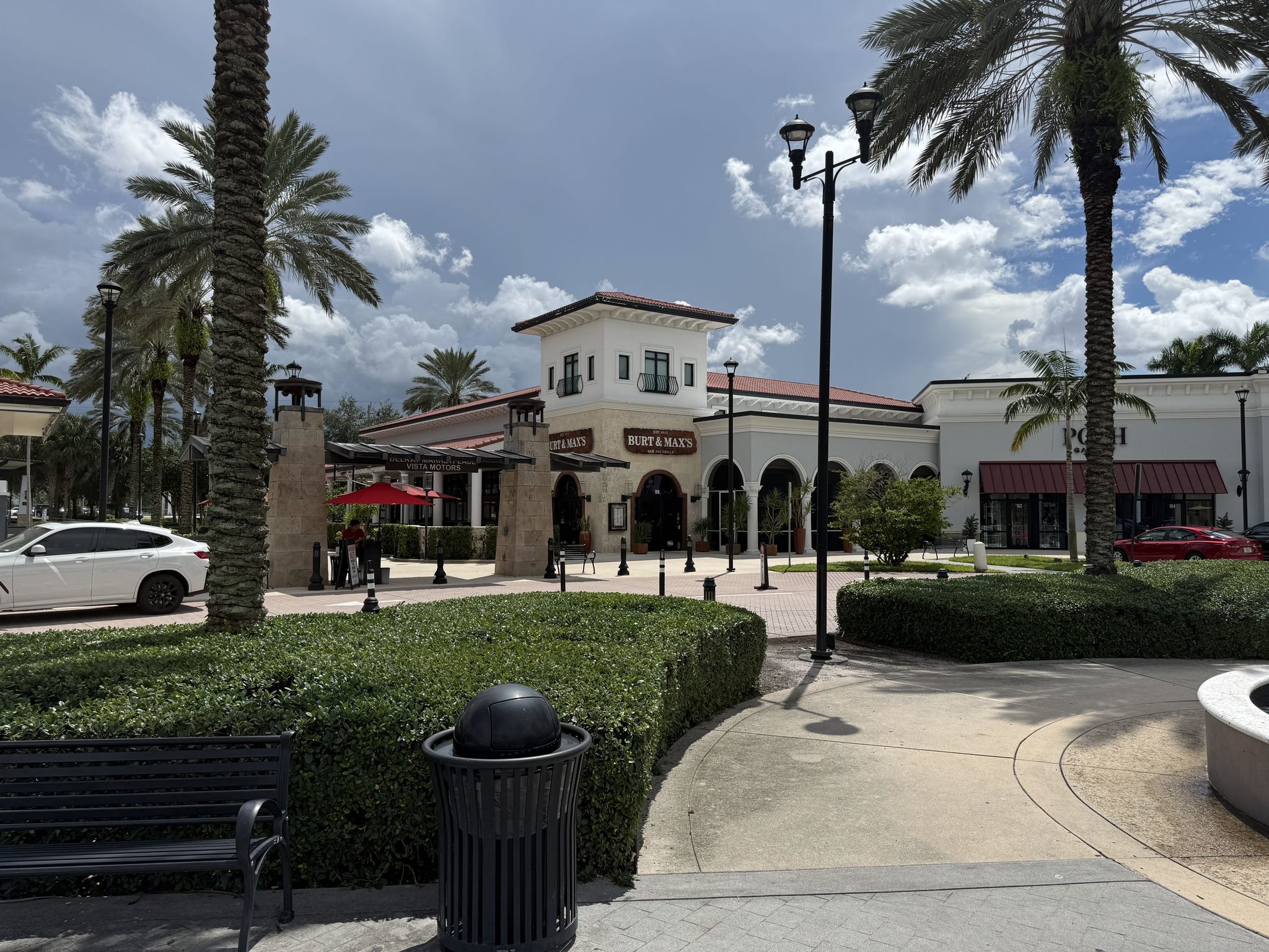 Burt & Max's at Delray Marketplace, a Mediterranean-style building with a tower, red umbrellas on the patio and palms in front