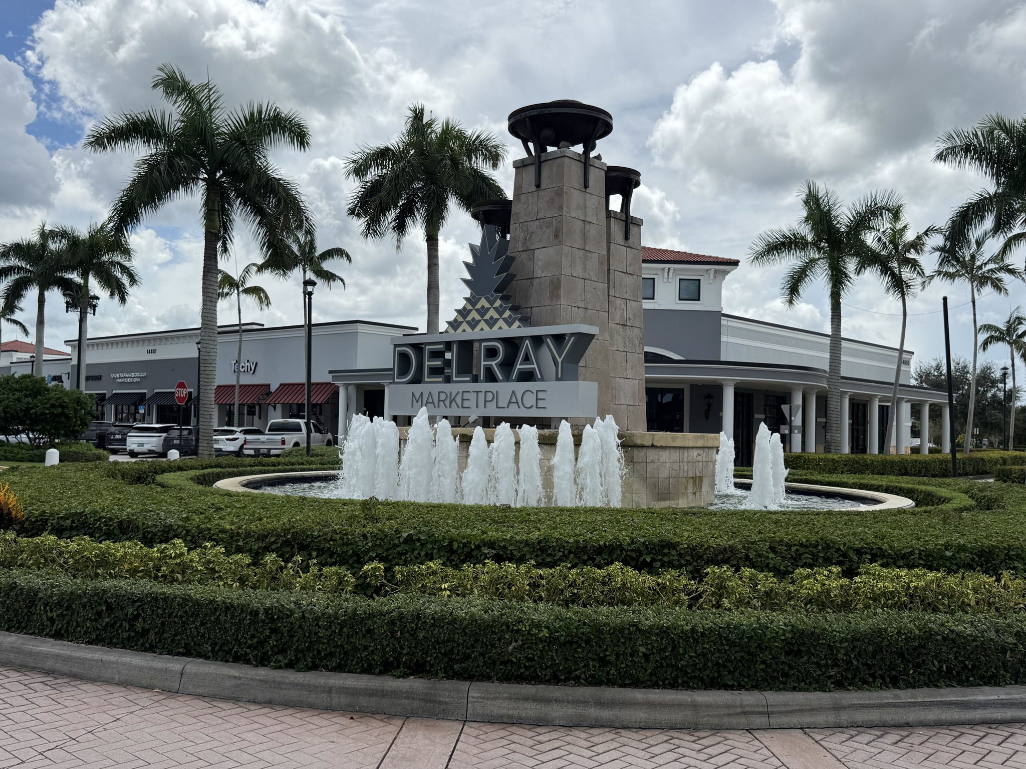 The Delray Marketplace entrance sign and fountain at the center's roundabout, with the Batch Local Kitchen building behind