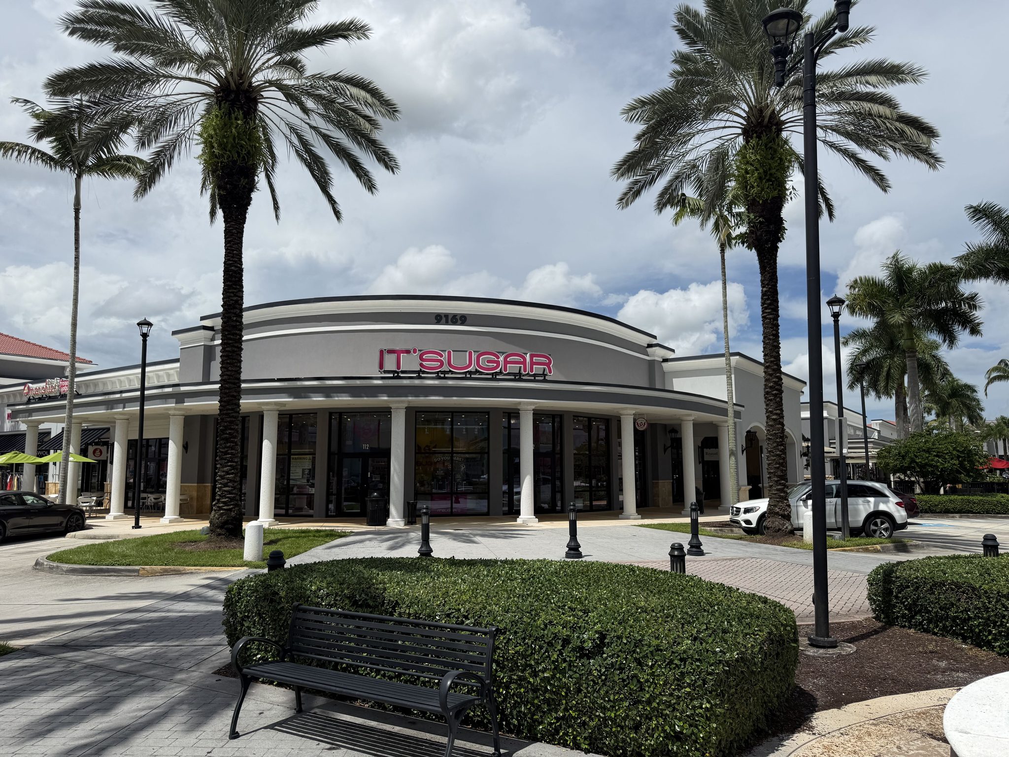 The IT'SUGAR storefront at Delray Marketplace, a curved white building with columns and a bench in front