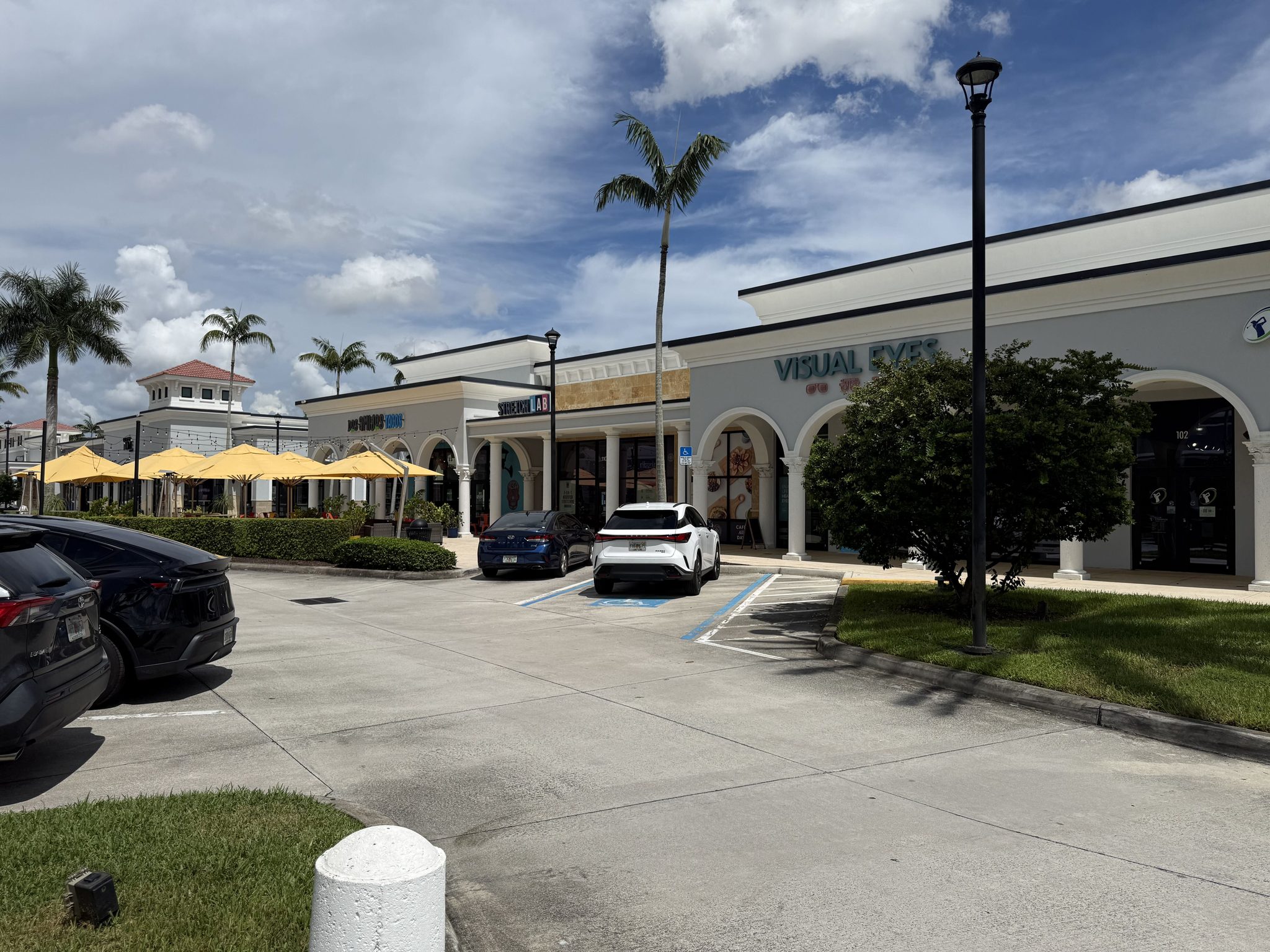 Yellow patio umbrellas over outdoor dining at Delray Marketplace, with shops and parking in front